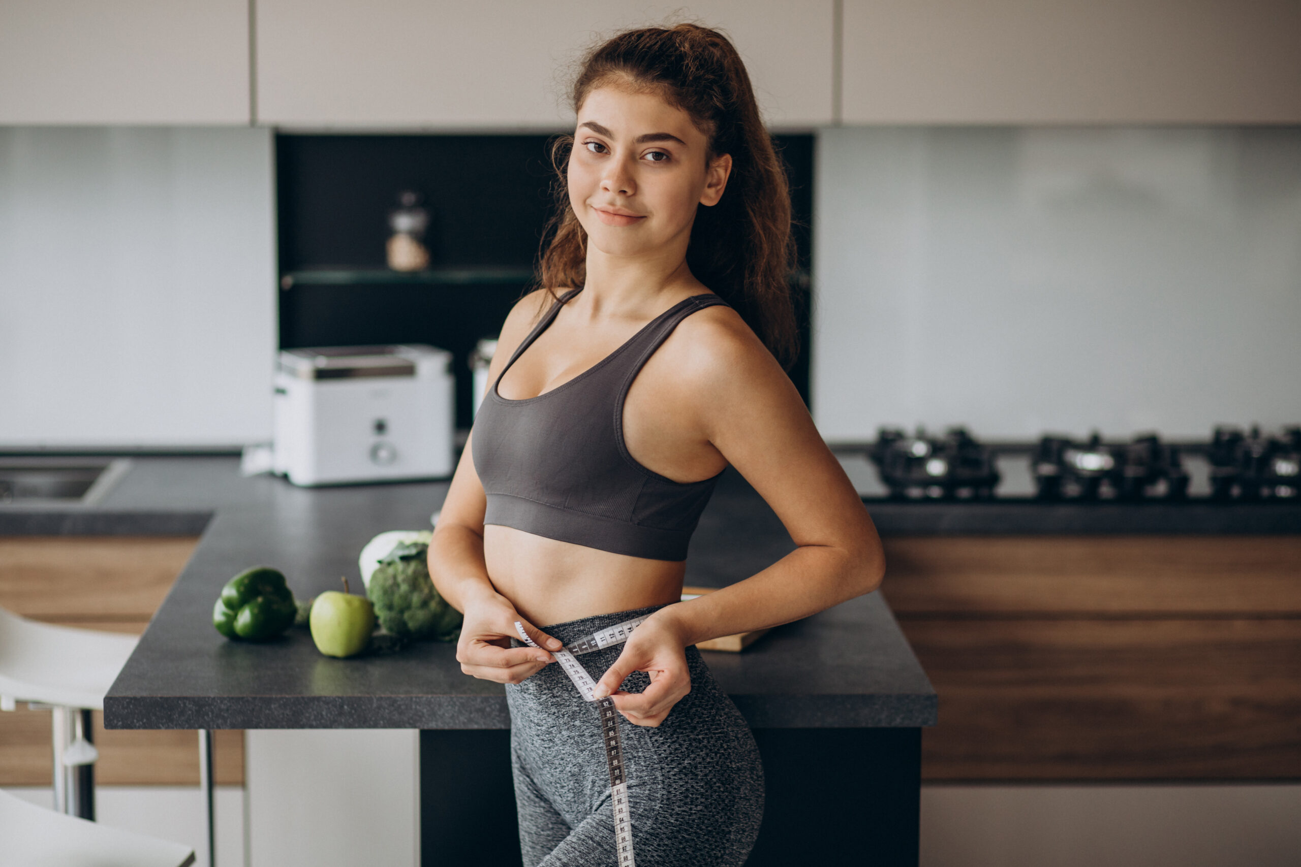 Young woman with measuting tape on weist at the kitchen